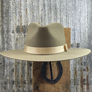 Brown mushroom hat with a gold band on a wooden block against a rustic metal wall.